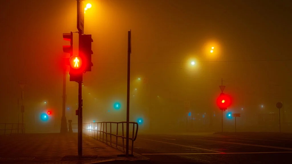 Los semáforos en un cruce parpadean en verde y rojo durante una noche brumosa.