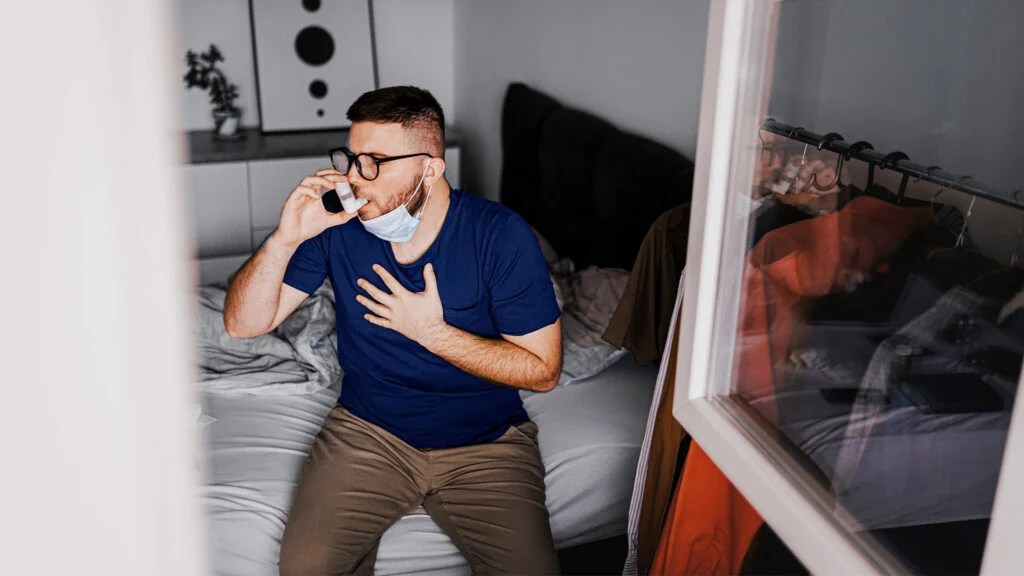 Un hombre en un dormitorio usando un inhalador para el asma no controlada.